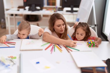 Teacher with boy and girl sitting on table drawing on paper at kindergarten