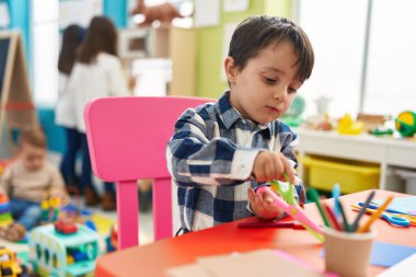 Adorable hispanic boy student holding scissors at kindergarten