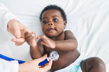 African american baby having medical examination lying on bed at bedroom