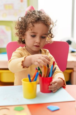 Adorable hispanic toddler student sitting on table drawing on paper at kindergarten