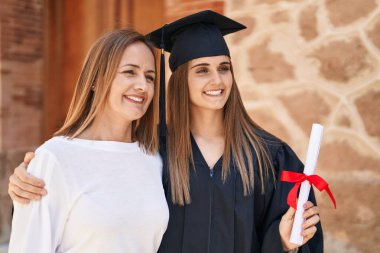 Two women mother and graduated daughter standing together at campus university