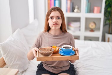 Redhead woman wearing pajama holding breakfast tray skeptic and nervous, frowning upset because of problem. negative person. 