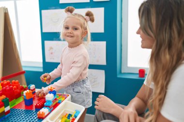 Teacher and toddler playing with construction blocks sitting on table at kindergarten