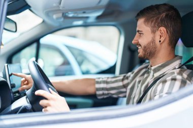 Sokakta bilgisayar GPS 'ine dokunarak araba kullanan beyaz bir genç.