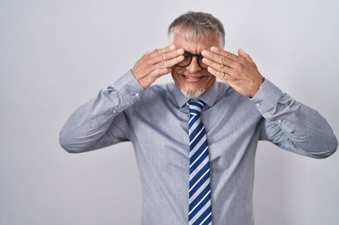 Hispanic business man with grey hair wearing glasses covering eyes with hands smiling cheerful and funny. blind concept. 