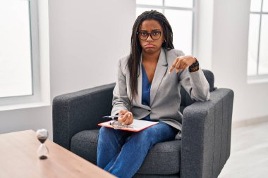 Young african american with braids working at consultation office pointing down looking sad and upset, indicating direction with fingers, unhappy and depressed. 