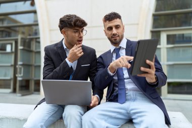 Two hispanic men business workers using touchpad and laptop working at street
