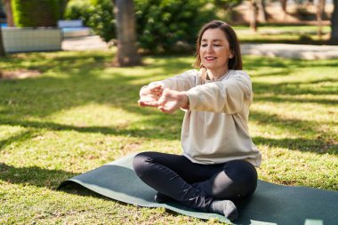 Orta yaşlı bir kadın parkta gerinirken kendine güvenerek gülümsüyor.