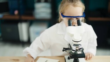 Adorable blonde girl student using microscope at laboratory classroom