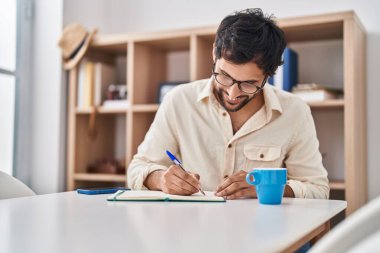 Young hispanic man writing on notebook at home