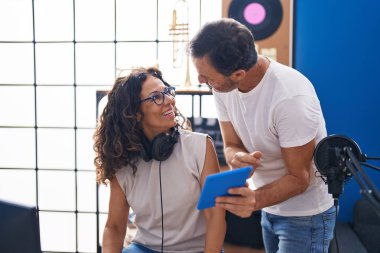 Man and woman musicians composing song using computer and touchpad at music studio