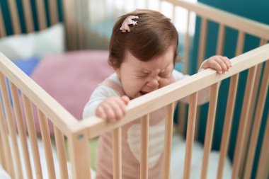 Adorable toddler standing on cradle crying at bedroom