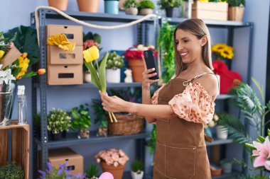 Genç ve güzel İspanyol çiçekçi çiçekçi çiçekçide çiçekçide akıllı telefonla fotoğraf çekiyor.