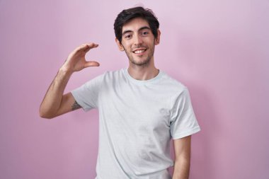Pembe arka planda duran, gülümseyen, kendine güvenen, el hareketi yapan, parmaklarıyla işaret yapan ve kameraya bakan genç İspanyol bir adam. ölçüm kavramı. 