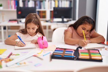 Two kids preschool students sitting on table drawing on paper at classroom