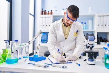 Laboratuvarda panoya yazı yazan, bilim adamı üniforması giyen İspanyol bir genç.