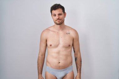 Young hispanic man standing shirtless wearing underware looking sleepy and tired, exhausted for fatigue and hangover, lazy eyes in the morning. 