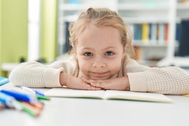 Adorable blonde girl student smiling confident leaning on book at classroom