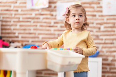 Adorable hispanic girl playing with construction blocks standing at kindergarten