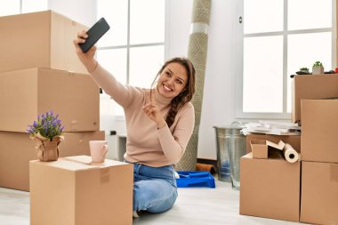 Genç ve güzel İspanyol kadın akıllı telefonuyla özçekim yapıyor. Yeni evinde yerde oturuyor.