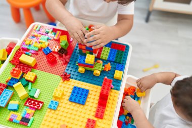 Adorable hispanic toddler playing with construction blocks sitting on table at kindergarten