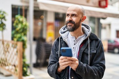 Sokakta akıllı telefon kullanarak kendine güvenen genç kel adam.