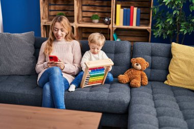 Mother and son using smartphone and playing with abacus at home