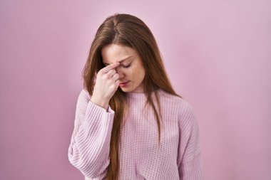 Pembe arka planda duran beyaz bir kadın yorgun burnu ve gözleri ovuşturup yorgunluk ve baş ağrısı çekiyor. Stres ve hüsran kavramı. 