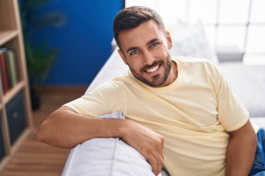 Evdeki kanepede kendinden emin gülümseyen İspanyol genç adam.