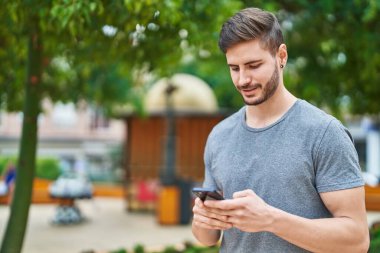 Parkta akıllı telefon kullanarak kendine güvenen beyaz bir genç.