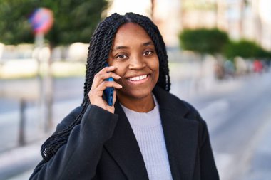 Afro-Amerikalı kadın gülümsüyor. Akıllı telefondan konuşuyor.