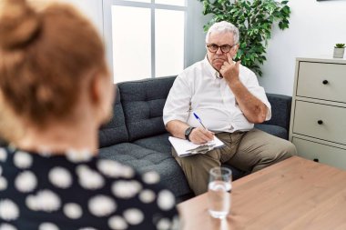 Senior psychologist man at consultation office pointing to the eye watching you gesture, suspicious expression 
