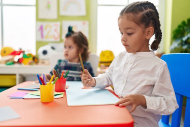Erkek ve kız kardeş öğrencileri anaokulunda masaya oturup kağıt çiziyorlar.