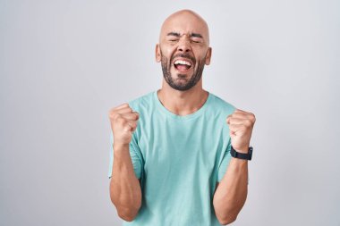 Middle age bald man standing over white background excited for success with arms raised and eyes closed celebrating victory smiling. winner concept. 