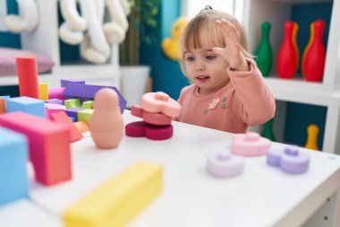 Adorable blonde girl playing with construction blocks sitting on table at kindergarten