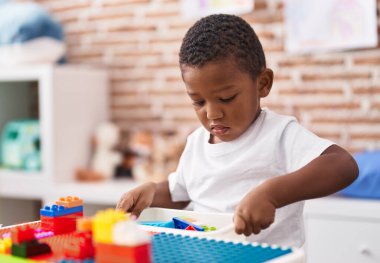 Anaokulundaki masada oturan Afrikalı Amerikalı çocuk inşaat bloklarıyla oynuyor.