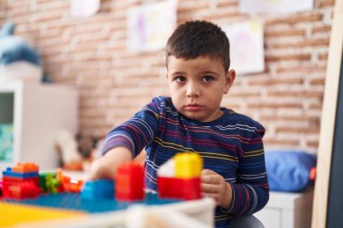 Adorable hispanic toddler playing with construction blocks sitting on table at kindergarten