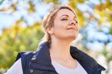 Parkta gözleri kapalı nefes alan genç sarışın kadın.