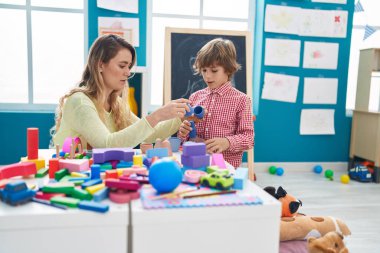 Teacher and toddler playing with geometry blocks sitting on table at kindergarten