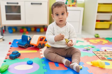 Anaokulunda yerde oturmuş maraca oynayan sevimli İspanyol çocuk.