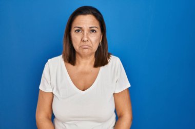 Hispanic mature woman standing over blue background depressed and worry for distress, crying angry and afraid. sad expression. 