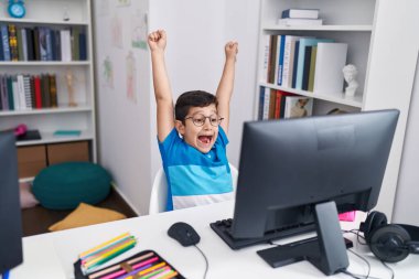 Adorable hispanic boy student using laptop with cheerful expression at classroom