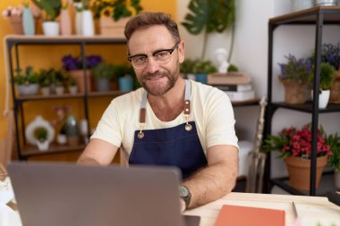 Middle age man florist smiling confident using laptop at flower shop