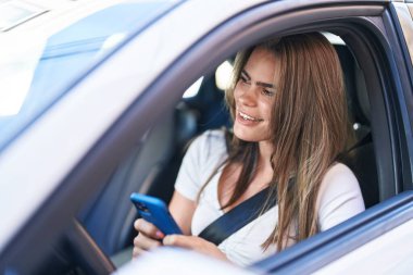 Young woman using smartphone sitting on car at street