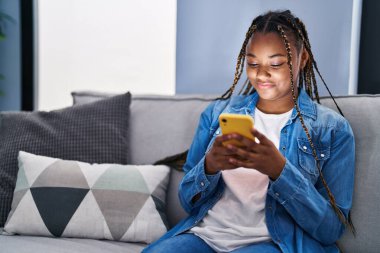 Evdeki koltukta oturan Afro-Amerikan kadın akıllı telefon kullanıyor