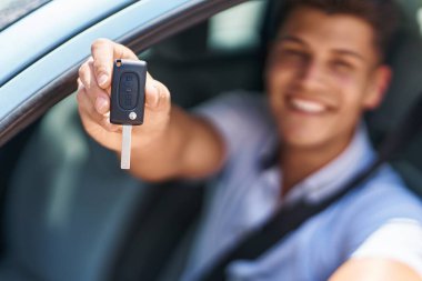 Young hispanic man smiling confident holding key of new car at street