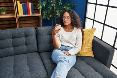 Genç Latin kadın evdeki kanepede oturmuş şampanya içiyor.