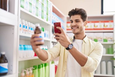 Young hispanic man customer make photo by smartphone to medicine bottle at pharmacy