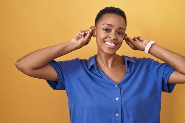 Sarı Arka Planda Dikilen Afrikalı Amerikalı Kadın Gülümsüyor Parmaklarıyla Kulaklarını — Stok fotoğraf