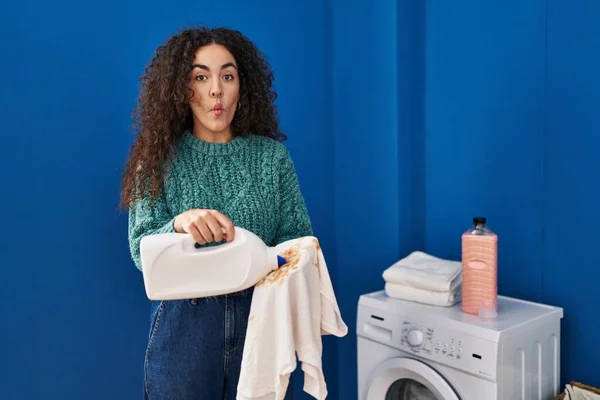 Young Hispanic Woman Holding Dirty Laundry Detergent Bottle Making Fish — Stockfoto